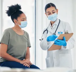 Doctor in white coat with gloves holding clipboard consulting patient about autoimmune testing.